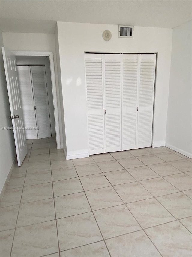 unfurnished bedroom featuring light tile patterned floors, baseboards, a closet, and visible vents