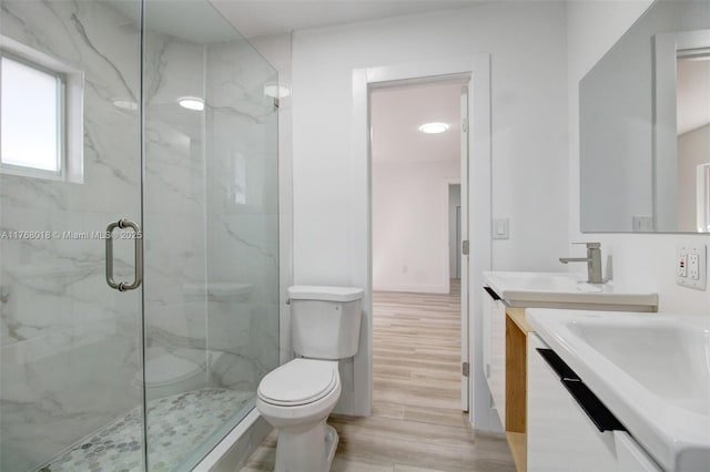 bathroom with a marble finish shower, toilet, vanity, and wood finished floors