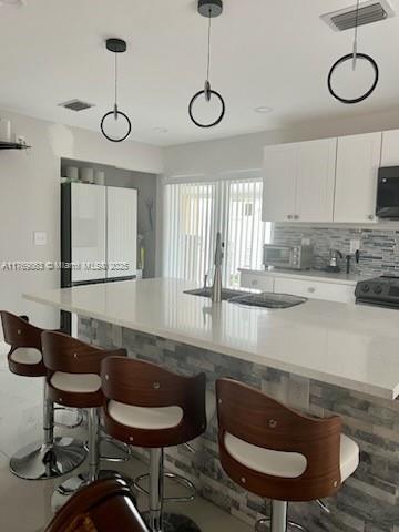 kitchen with backsplash, a sink, visible vents, white cabinets, and black microwave