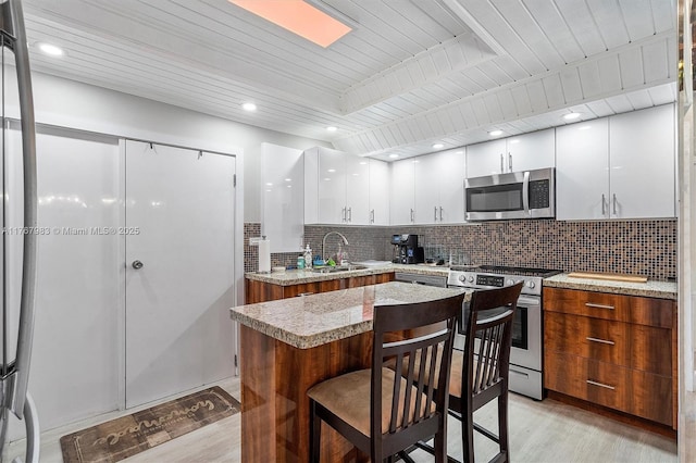 881 Hialeah Dr, Hialeah, FL 33010 - kitchen featuring appliances with stainless steel finishes, light wood-style floors, white cabinets, decorative backsplash, and a breakfast bar area