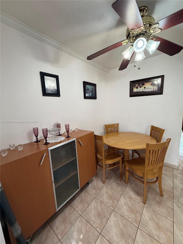 dining space with light tile patterned floors, ceiling fan, ornamental molding, and a textured ceiling