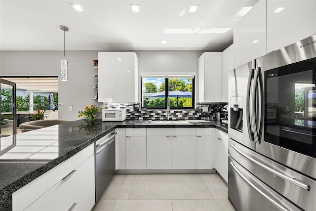 6166 Pine Tree Dr, Miami Beach, FL 33140 - kitchen with appliances with stainless steel finishes, white cabinetry, light tile patterned floors, and tasteful backsplash