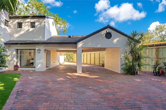 rear view of house with a tile roof, an attached carport, stucco siding, fence, and decorative driveway