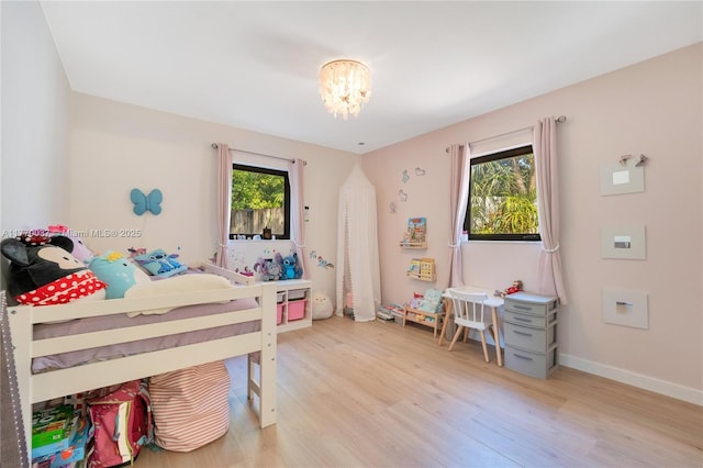 bedroom with multiple windows, light wood-style flooring, baseboards, and an inviting chandelier