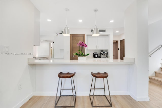 kitchen featuring a breakfast bar, white cabinetry, light countertops, and a peninsula