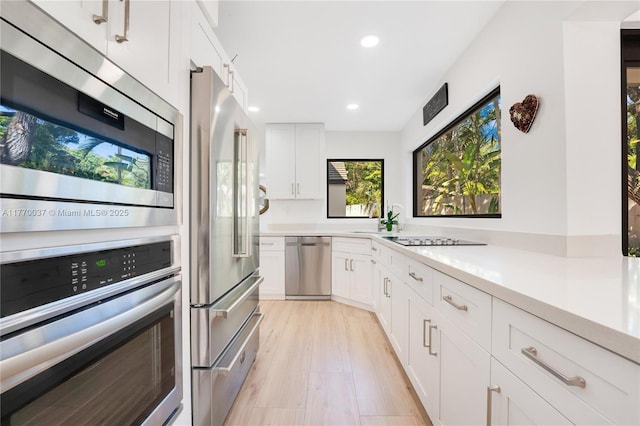 kitchen with light countertops, recessed lighting, light wood finished floors, white cabinets, and appliances with stainless steel finishes