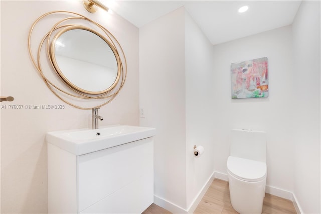 half bathroom with baseboards, wood finished floors, toilet, recessed lighting, and vanity