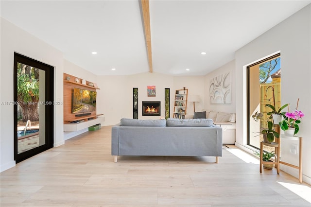 living area with light wood-style flooring, a glass covered fireplace, beamed ceiling, and recessed lighting