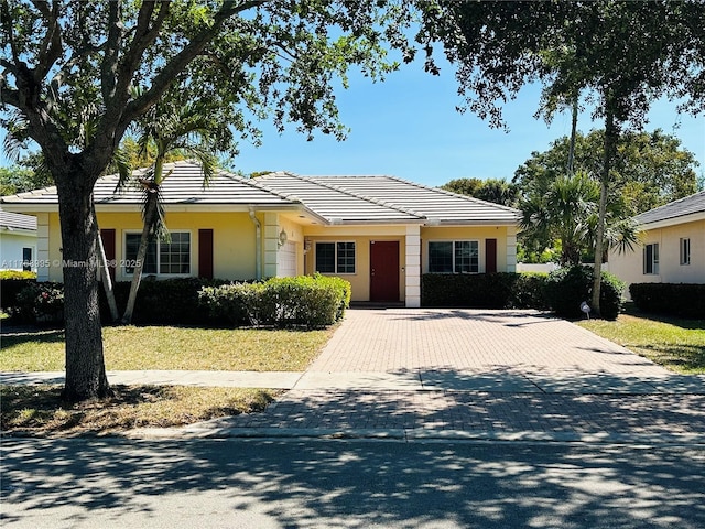ranch-style home with a tile roof, decorative driveway, and stucco siding