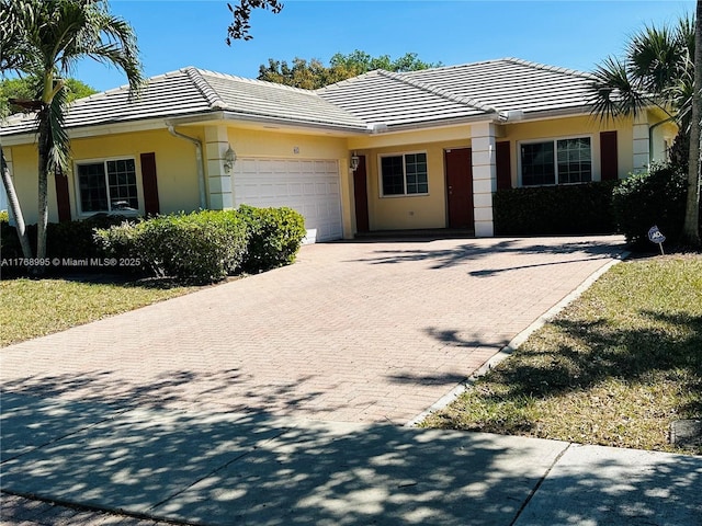 single story home with an attached garage, a tile roof, stucco siding, and decorative driveway