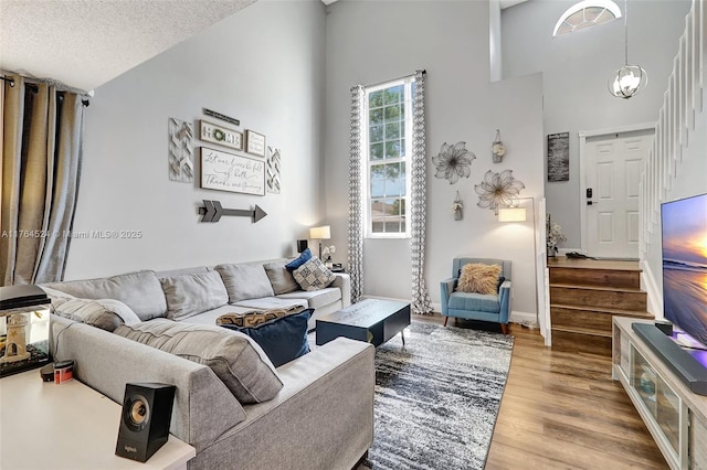 living area featuring stairs, a textured ceiling, wood finished floors, and a towering ceiling