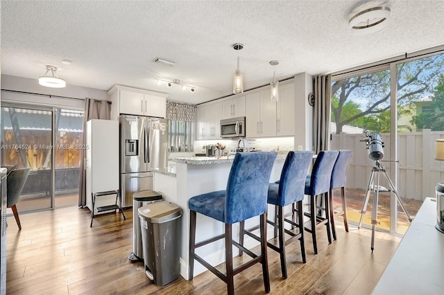 kitchen featuring white cabinetry, wood finished floors, a kitchen breakfast bar, appliances with stainless steel finishes, and hanging light fixtures