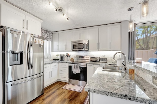 kitchen with dark wood-style flooring, stainless steel appliances, a sink, white cabinets, and a peninsula