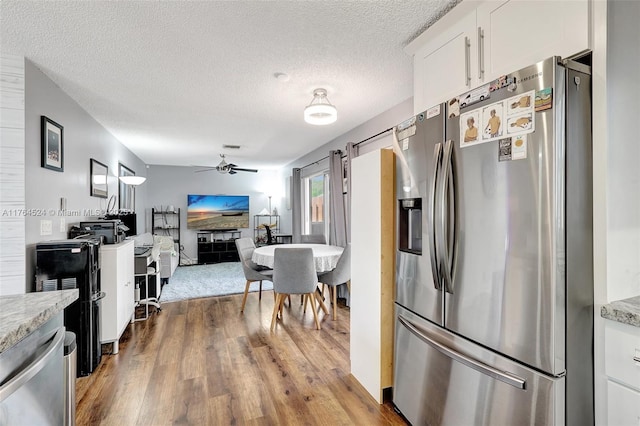 kitchen featuring wood finished floors, stainless steel fridge, a textured ceiling, white cabinets, and ceiling fan