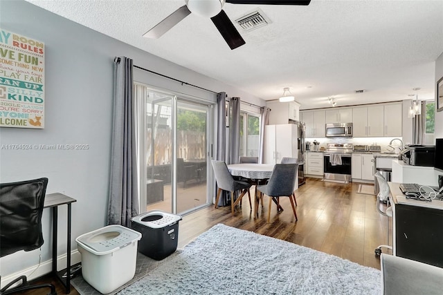 dining area with wood finished floors, a textured ceiling, ceiling fan, and visible vents