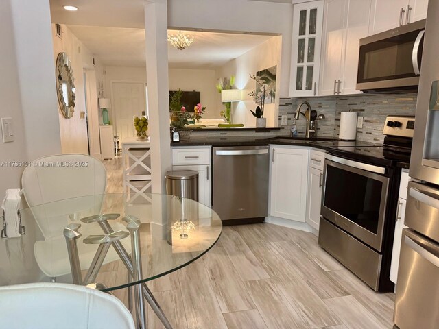 kitchen with white cabinetry, stainless steel appliances, backsplash, and dark countertops