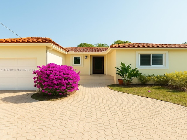 mediterranean / spanish house featuring a garage, a tiled roof, decorative driveway, and stucco siding