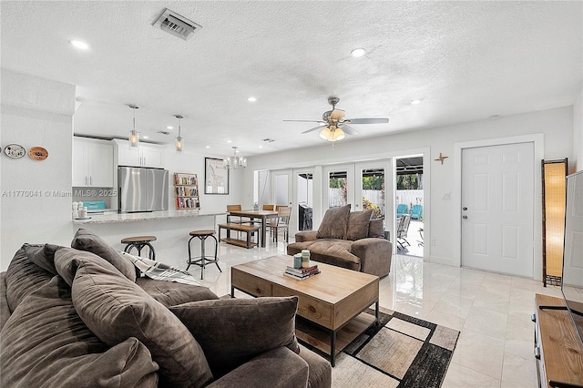living area featuring a textured ceiling, ceiling fan with notable chandelier, visible vents, and recessed lighting