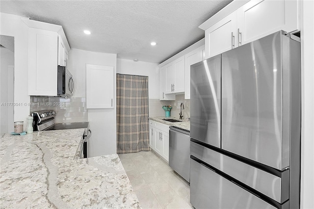 kitchen with a sink, appliances with stainless steel finishes, light stone counters, and white cabinetry