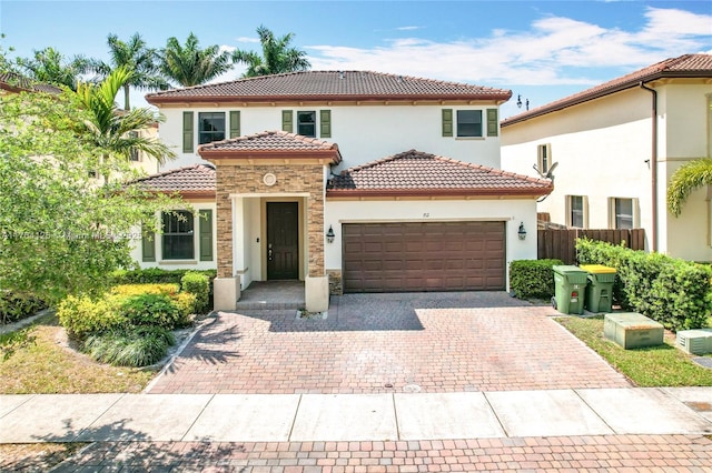 mediterranean / spanish-style home with stucco siding, decorative driveway, fence, a tile roof, and an attached garage