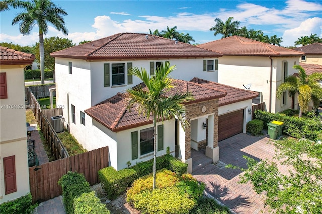 mediterranean / spanish house featuring central air condition unit, stucco siding, an attached garage, a tile roof, and fence