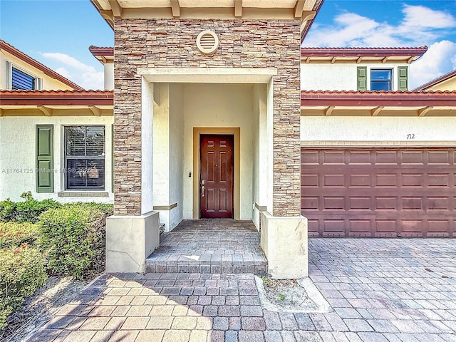 view of exterior entry with an attached garage, stucco siding, and stone siding