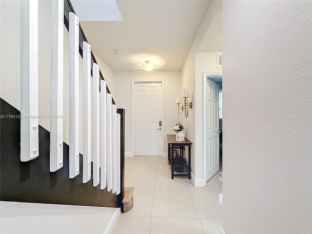 foyer featuring baseboards, light tile patterned floors, a textured wall, and visible vents