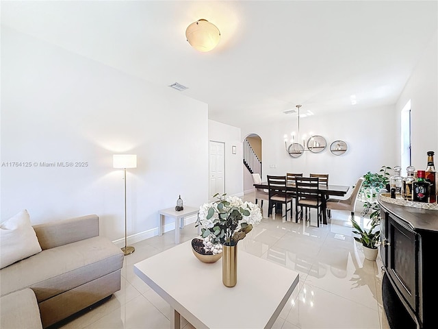 living room featuring visible vents, baseboards, light tile patterned floors, arched walkways, and a notable chandelier