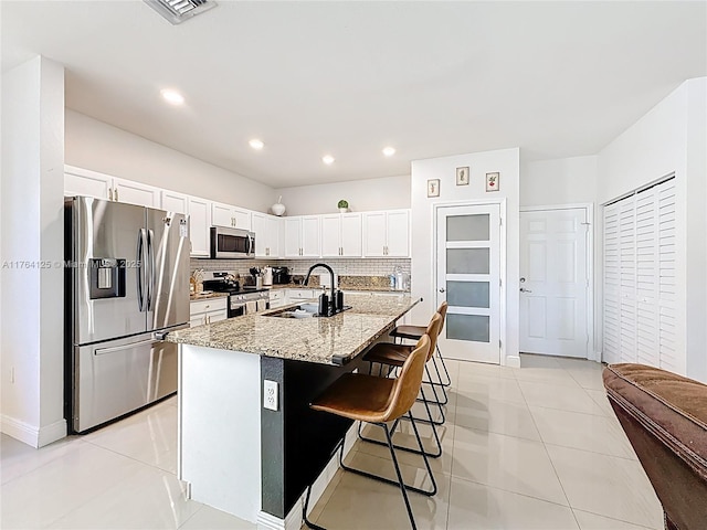 kitchen featuring light tile patterned flooring, a sink, stainless steel appliances, a breakfast bar area, and backsplash