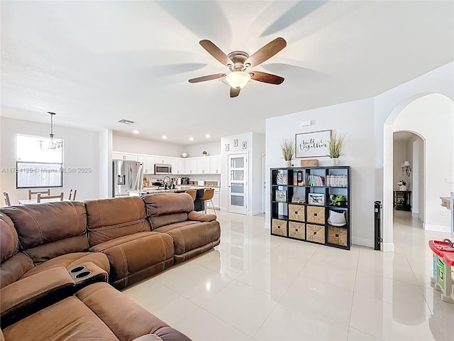 living room with arched walkways, ceiling fan with notable chandelier, light tile patterned floors, and visible vents