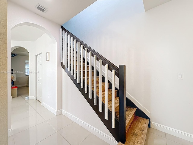 stairs with arched walkways, baseboards, tile patterned flooring, and visible vents