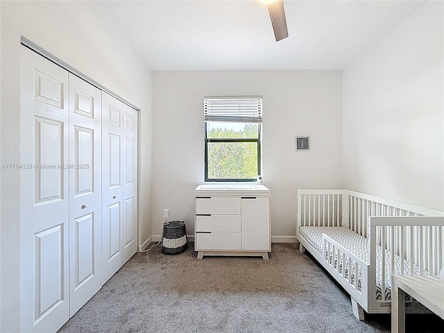 carpeted bedroom featuring a nursery area, a closet, baseboards, and ceiling fan