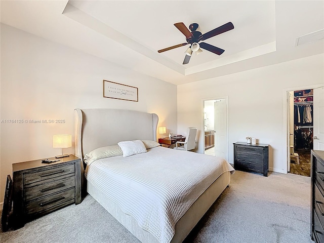 bedroom featuring light carpet, a ceiling fan, connected bathroom, a walk in closet, and a tray ceiling