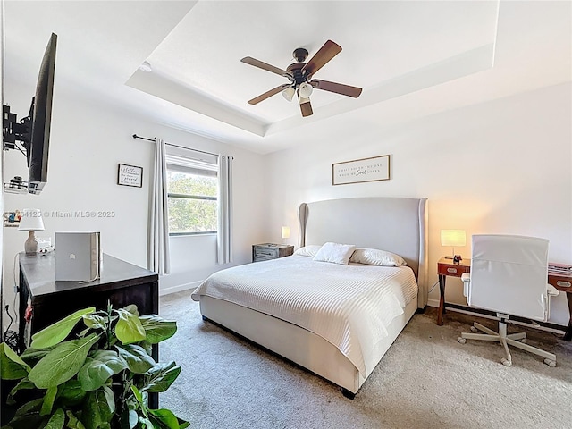 carpeted bedroom featuring a tray ceiling, ceiling fan, and baseboards