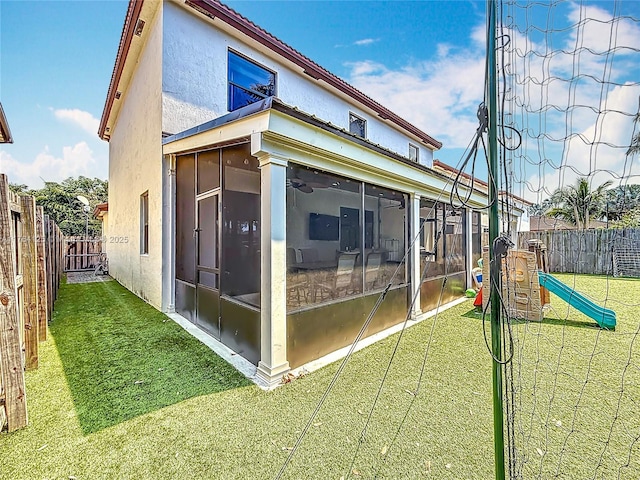 exterior space featuring a sunroom, a yard, a fenced backyard, a playground, and stucco siding