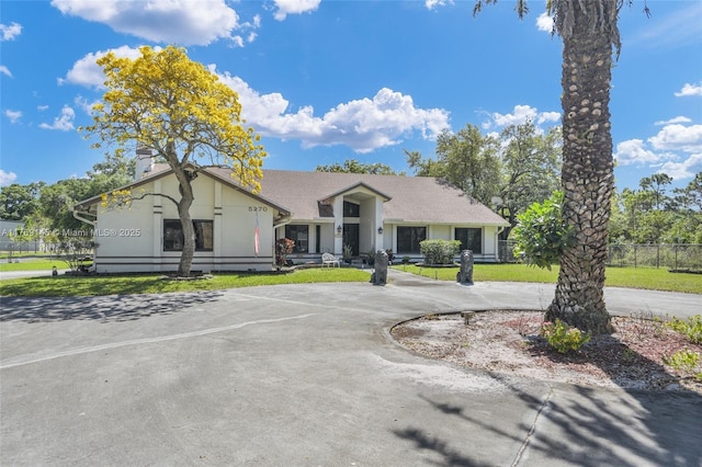 view of front of property with curved driveway, stucco siding, fence, and a front lawn
