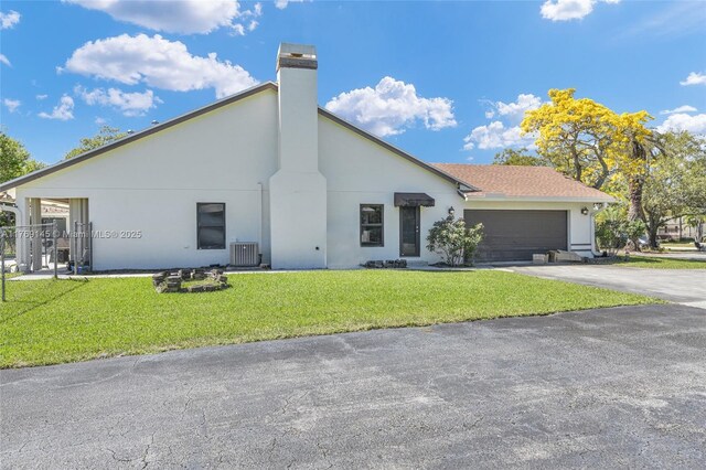 view of front of property with concrete driveway, an attached garage, central AC unit, a front lawn, and a chimney