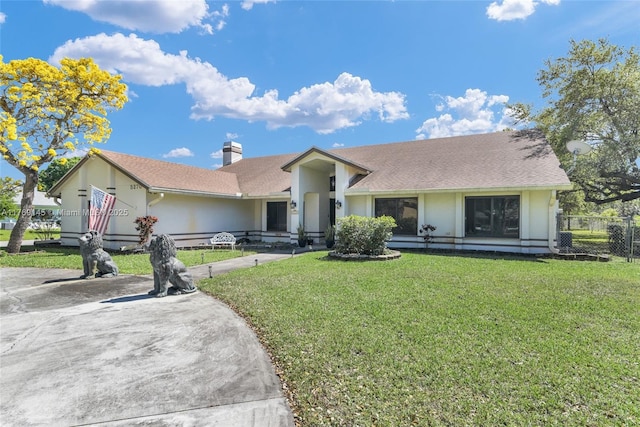 view of front facade with driveway, a front yard, a chimney, stucco siding, and fence