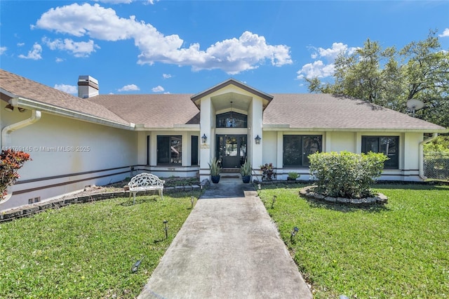 view of front of house with a chimney, a front yard, stucco siding, and roof with shingles