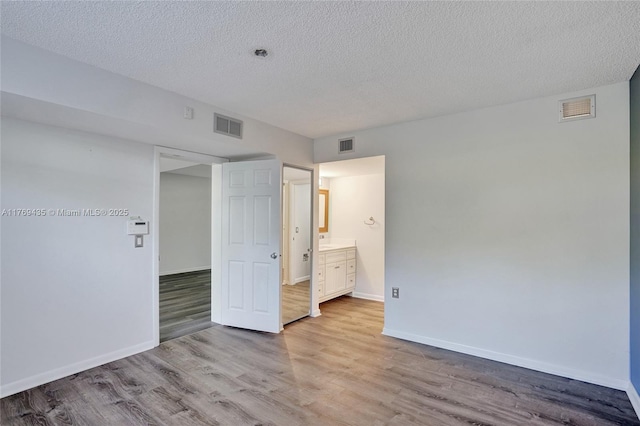 unfurnished bedroom with a textured ceiling, visible vents, and wood finished floors