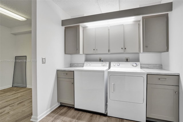clothes washing area with light wood-style floors, baseboards, a textured ceiling, cabinet space, and independent washer and dryer