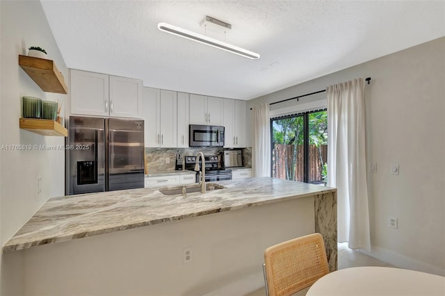 kitchen with a sink, stainless steel appliances, a kitchen bar, light stone countertops, and backsplash
