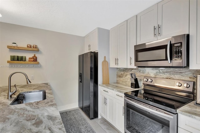 kitchen with open shelves, a sink, stainless steel appliances, baseboards, and light stone countertops