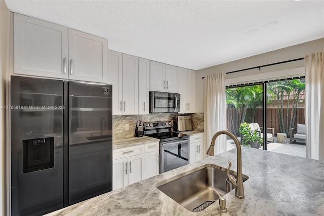 kitchen with white cabinetry, tasteful backsplash, a sink, appliances with stainless steel finishes, and light stone countertops