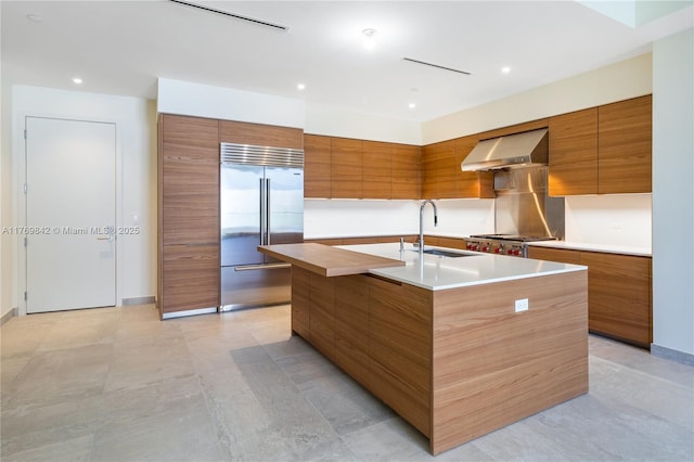 kitchen featuring modern cabinets, wall chimney exhaust hood, stainless steel built in refrigerator, and brown cabinetry