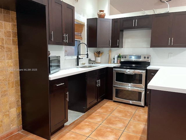 kitchen with light countertops, stainless steel appliances, dark brown cabinets, a sink, and light tile patterned floors