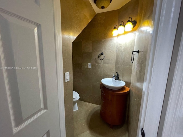 half bath with tile walls, toilet, tile patterned flooring, and vanity