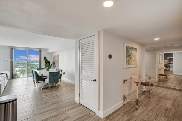 hallway featuring light wood-style flooring, baseboards, expansive windows, and recessed lighting