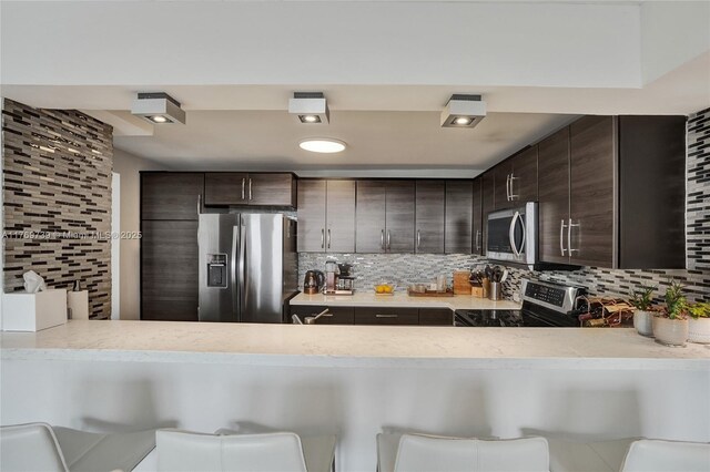 10000 W Bay Harbor Dr Unit Ph23, Bay Harbor Islands, FL 33154 - kitchen featuring appliances with stainless steel finishes, dark brown cabinetry, a peninsula, and tasteful backsplash