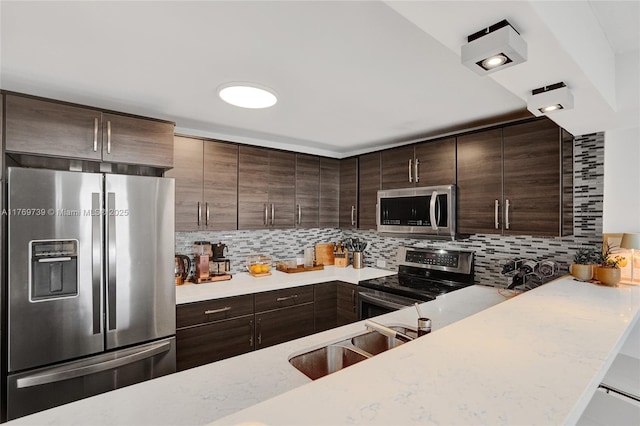 kitchen featuring light stone counters, a sink, stainless steel appliances, decorative backsplash, and dark brown cabinets